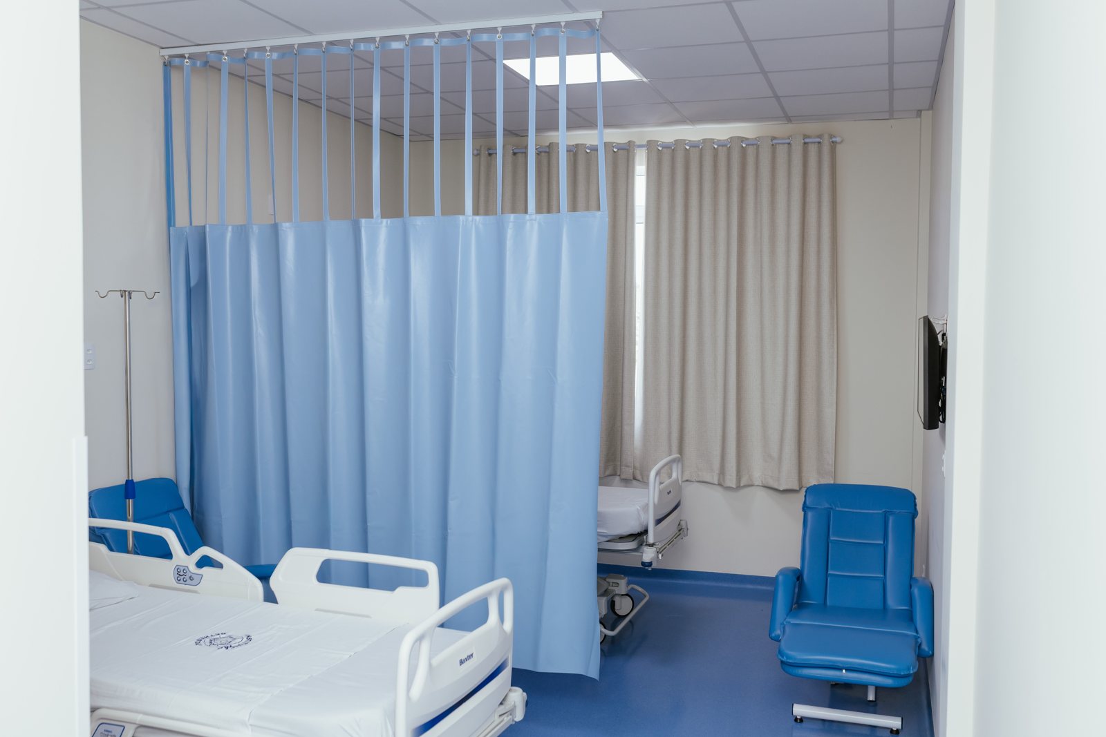 Cortina hospitalar azul em quarto com leito e poltrona